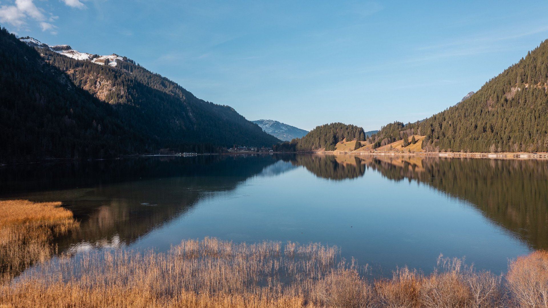 Hotel Sonnenhof See mit braunen Schilfgrasfeldern und bewaldeten Bergen bei klarem Himmel