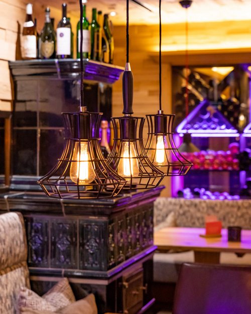 Hotel Sonnenhof Warme Hängeleuchten über Holztisch in gemütlicher Bar mit Flaschenregal