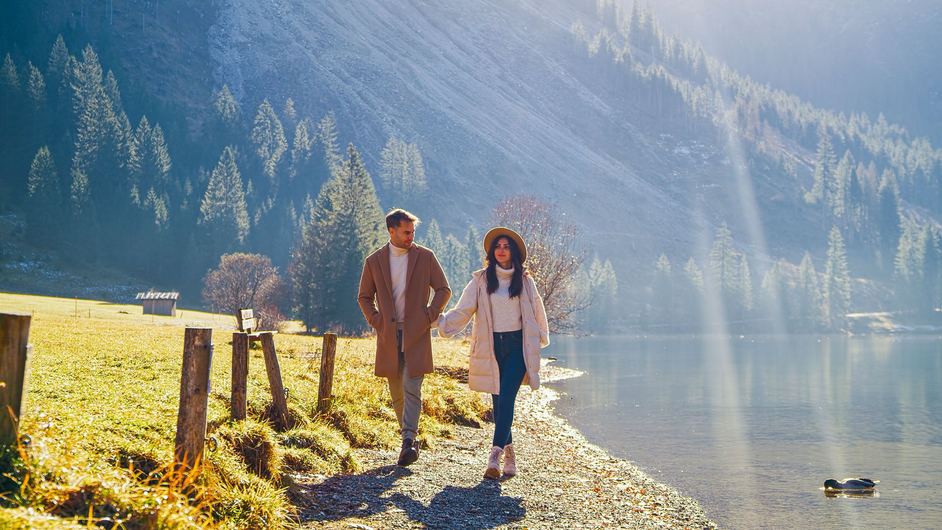 Hotel Sonnenhof Paar spaziert am Ufer eines Sees in sonniger Berglandschaft