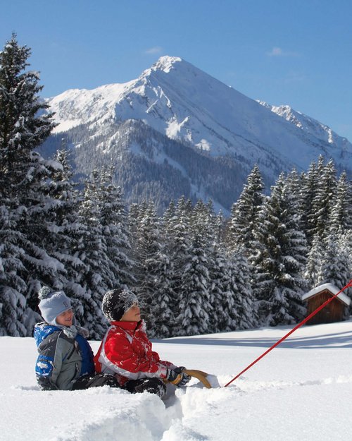 Hotel Sonnenhof Mann zieht Kinder auf Schlitten durch verschneite Winterlandschaft mit Bergen