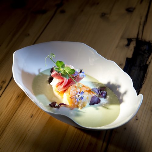 Hotel Sonnenhof Gourmetgericht mit Garnelen, Schinken und essbaren Blüten in weißer Schüssel auf Holztisch