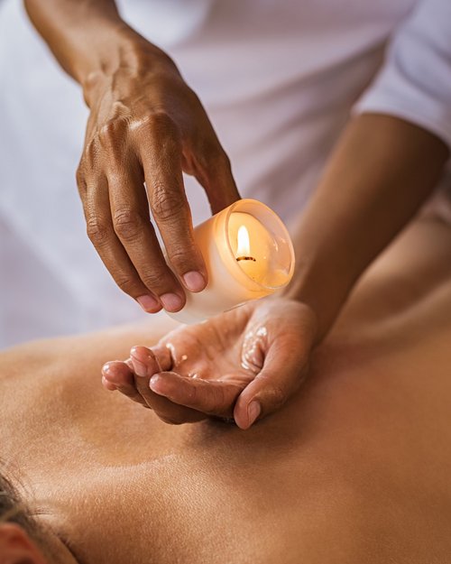 Hotel Sonnenhof Person gießt warmes Öl von einer Kerze für eine Rückmassage