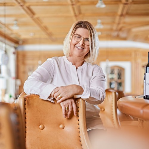 Hotel Sonnenhof Ältere Frau mit Brille sitzt lächelnd auf Ledersessel in gemütlichem Raum