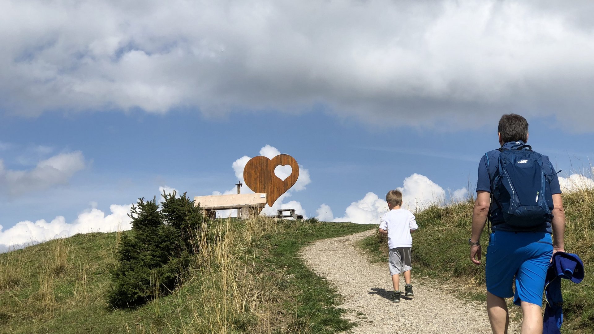 Hotel Sonnenhof Vater und Sohn wandern auf einem Weg zu einer Bank mit Herzskulptur auf einem Hügel