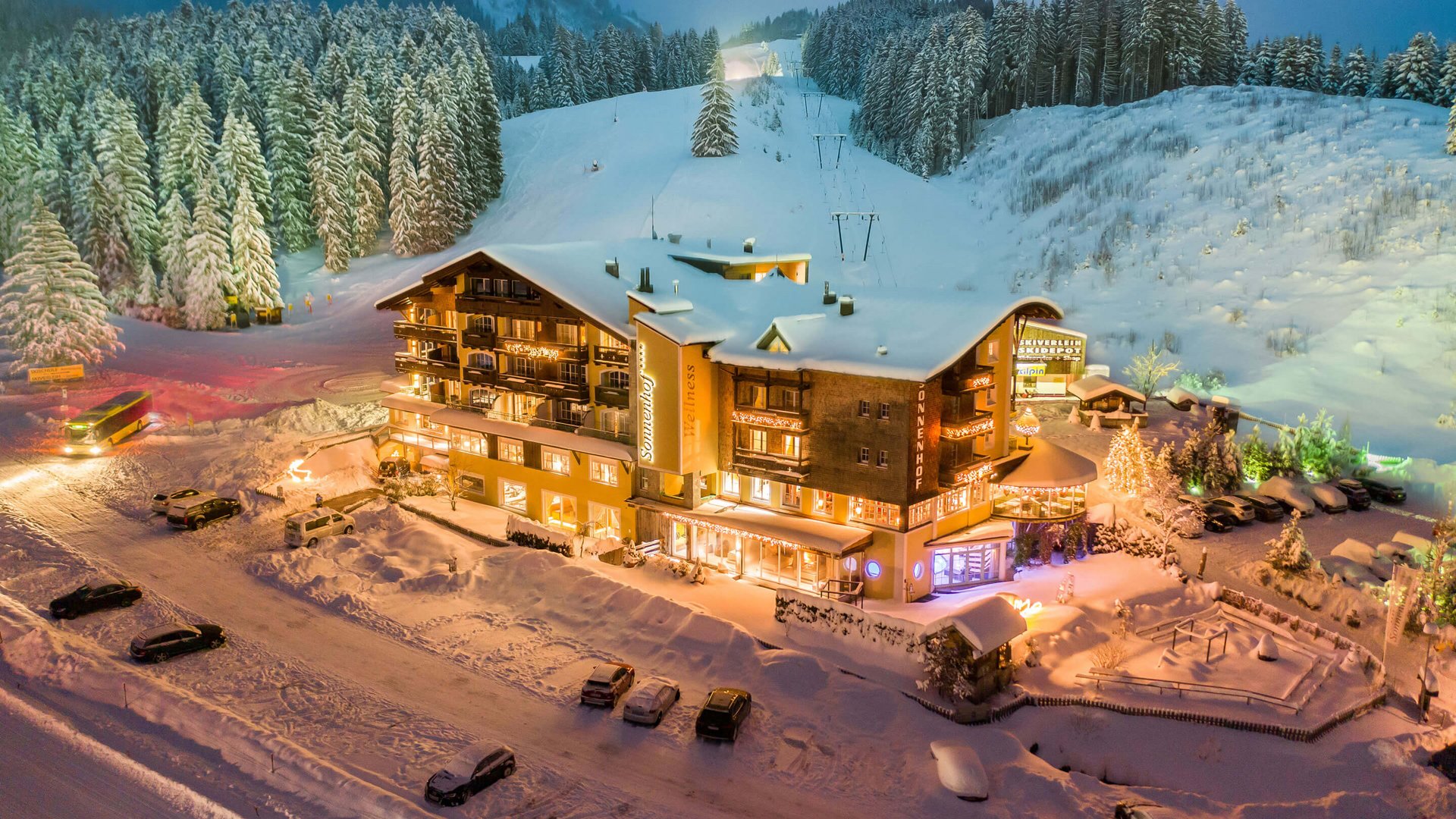 Hotel Sonnenhof Beleuchtetes Hotel in verschneiter Winterlandschaft am Abend mit Skilift und Wald