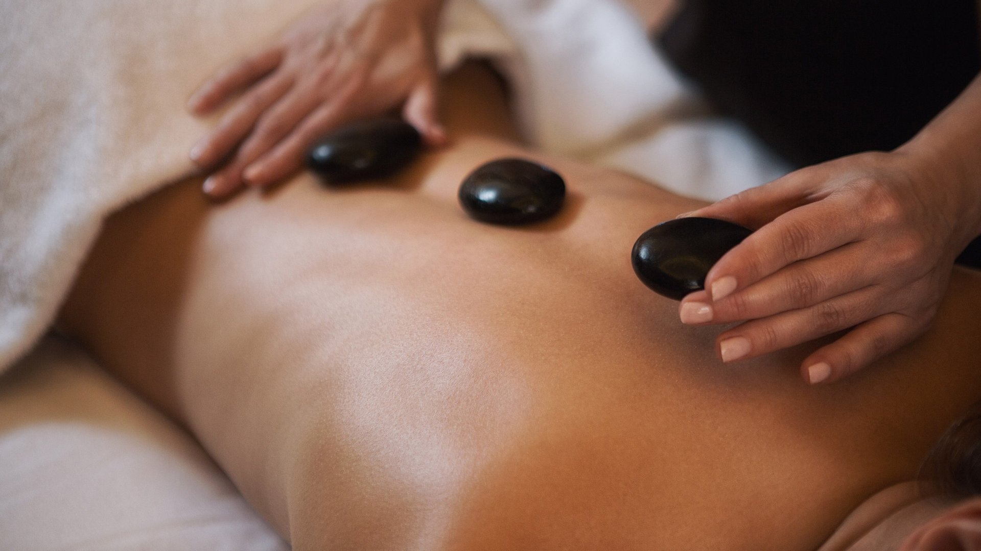 Hot-Stone-Massage mit Bergblick – Sky Spa im Sonnenhof Tirol, Grän Person erhält Hot-Stone-Massage auf nacktem Rücken