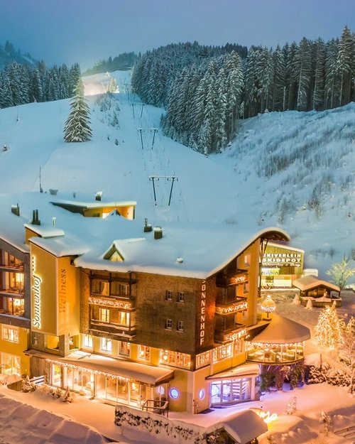 Hotel Sonnenhof Beleuchtetes Hotel im verschneiten Winterwald bei Nacht mit Skihang im Hintergrund