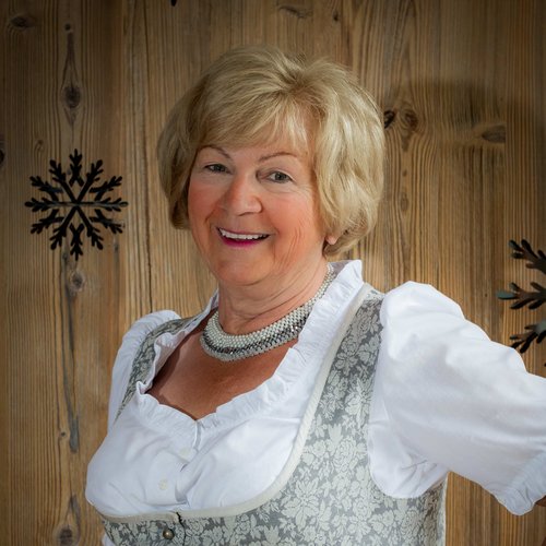Hotel Sonnenhof Ältere Frau in traditionellem Dirndl vor Holzwand mit Schneeflockendekor