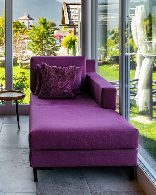 Hotel Sonnenhof Purpurfarbene Chaiselongue vor großem Fenster mit Bergblick