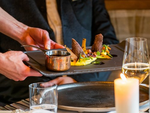Hotel Sonnenhof Kellner serviert kunstvoll angerichtetes Gericht auf schwarzem Teller im Restaurant