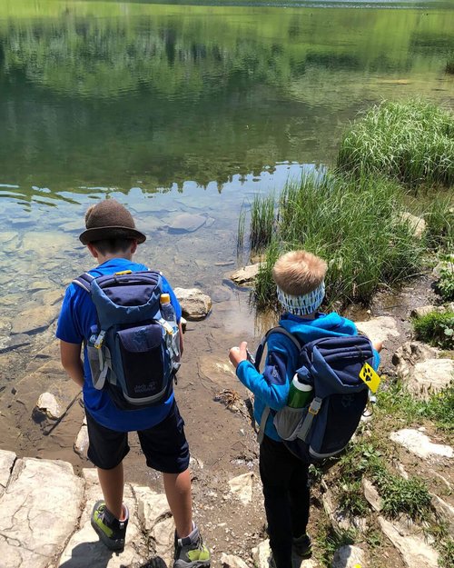 Hotel Sonnenhof Zwei Kinder mit Rucksäcken stehen am Ufer eines klaren Sees