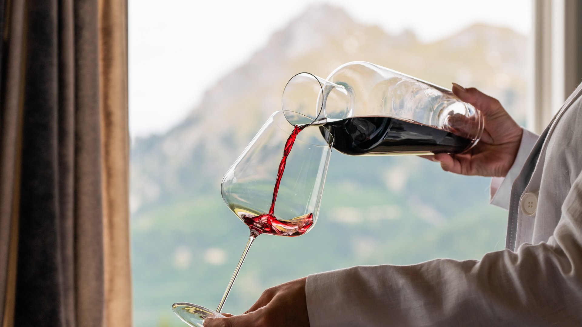 Hotel Sonnenhof Person gießt Rotwein aus Karaffe in Weinglas vor Bergkulisse