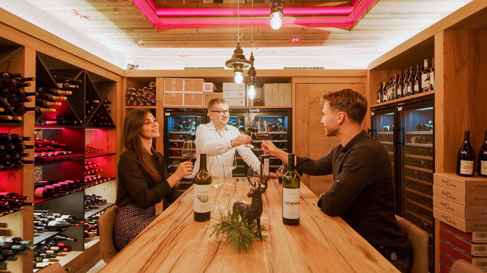 Hotel Sonnenhof Drei Personen stoßen mit Weingläsern in einem Holz-Weinkeller an