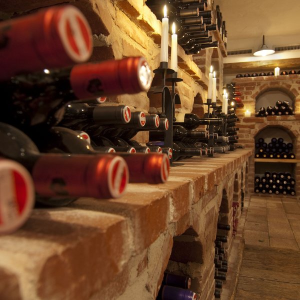 Hotel Sonnenhof Weinkeller mit roten Weinflaschen auf Ziegelregalen und brennenden Kerzen