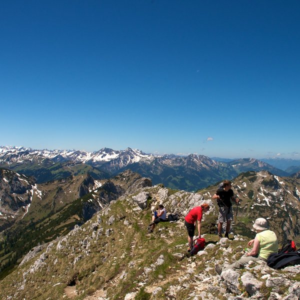 Hotel Sonnenhof Wanderer auf Gipfel mit Blick auf schneebedeckte Bergkette und blauen Himmel