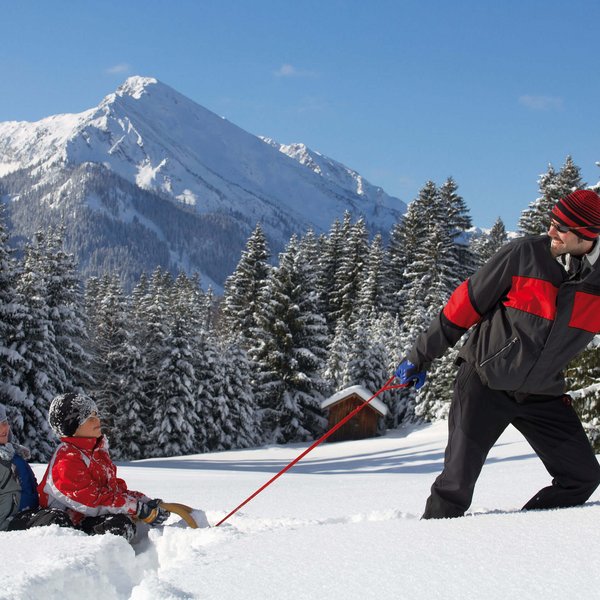 Hotel Sonnenhof Mann zieht Kinder auf Schlitten durch verschneite Winterlandschaft mit Bergen