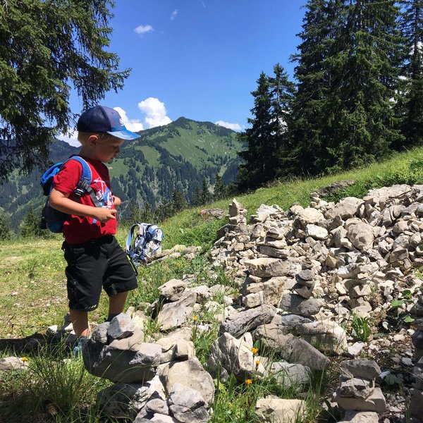 Hotel Sonnenhof Junge mit rotem T-Shirt schaut auf Steinmännchen am Bergweg bei sonnigem Wetter