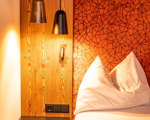 Hotel Sonnenhof Betthaupt mit rotem Muster, Nachttisch und zwei Hängelampen an Holzwand
