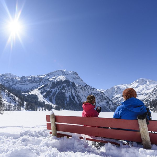 Hotel Sonnenhof Zwei Personen auf roter Bank genießen sonnige Schneelandschaft mit Bergen