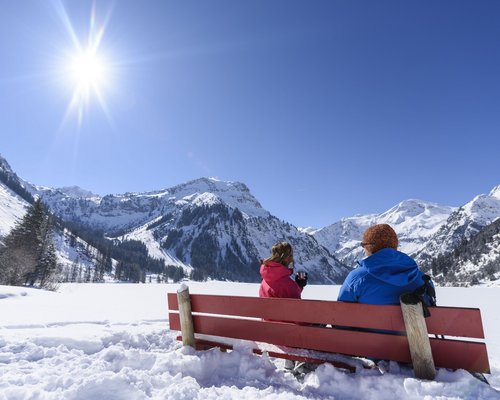 Hotel Sonnenhof Zwei Personen auf roter Bank genießen sonnige Schneelandschaft mit Bergen