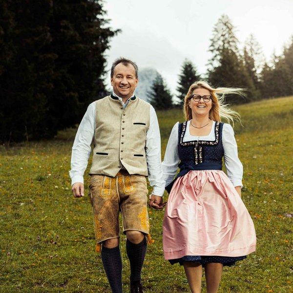Hotel Sonnenhof Paar in traditioneller Tracht geht Hand in Hand über eine Wiese