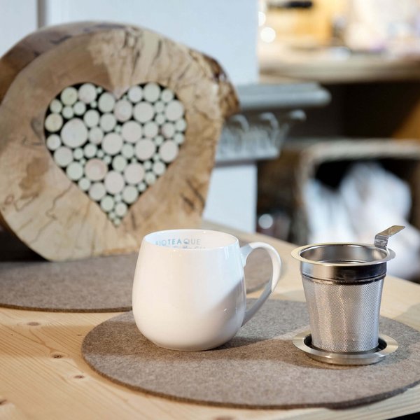 Hotel Sonnenhof Weiße Tasse und Teesieb auf einem Holztisch mit Herz-Dekoration aus Holzscheiben