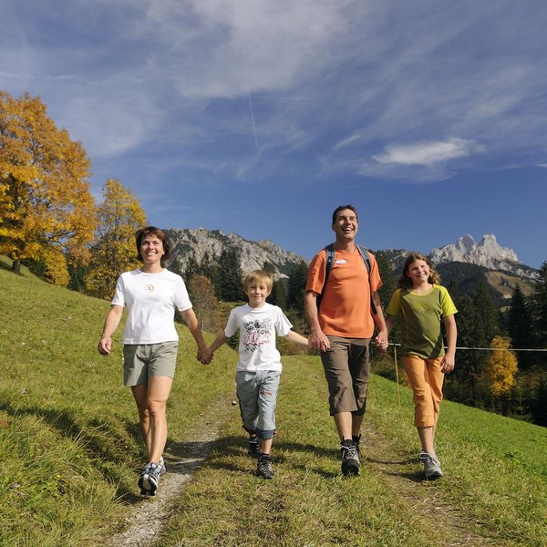 Hotel Sonnenhof Familie wandert glücklich auf einem Bergweg mit Herbstbäumen und Bergen im Hintergrund