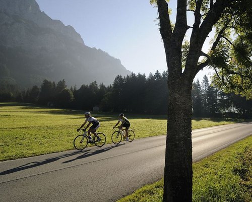Hotel Sonnenhof Zwei Radfahrer fahren auf einer Landstraße neben Bäumen und Bergen bei Sonnenlicht