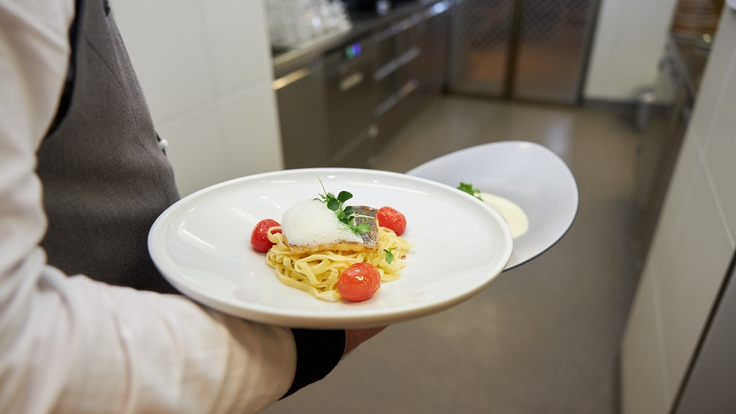 Hotel Sonnenhof Kellner trägt Teller mit Pasta, gebratenem Fisch und Tomaten in Restaurantküche