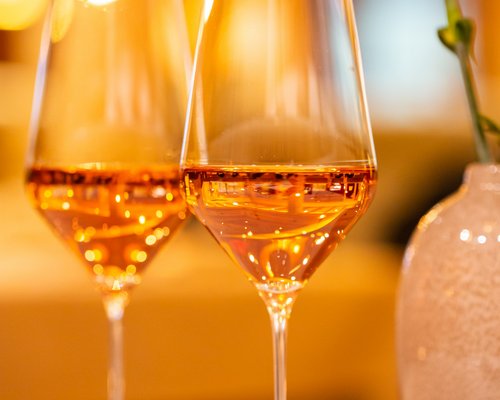 Hotel Sonnenhof Zwei Gläser mit rosé Wein neben einer Vase mit rosa Blume