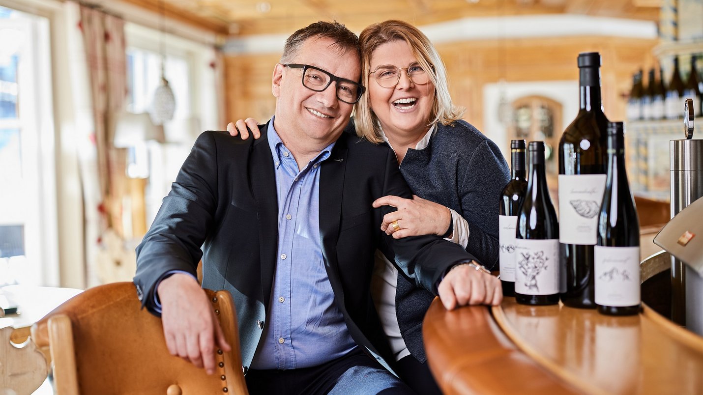 Hotel Sonnenhof Lächelndes Paar sitzt an Bar mit Weinflaschen in gemütlichem Raum