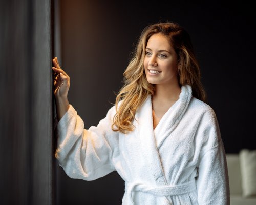 Hotel Sonnenhof Frau im weißen Bademantel blickt lächelnd aus einem Fenster