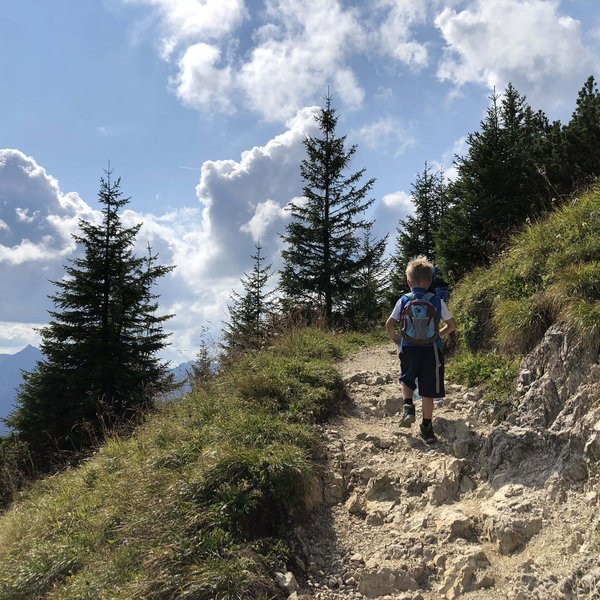 Hotel Sonnenhof Kind wandert auf felsigem Bergweg mit Kiefern und bewölktem Himmel