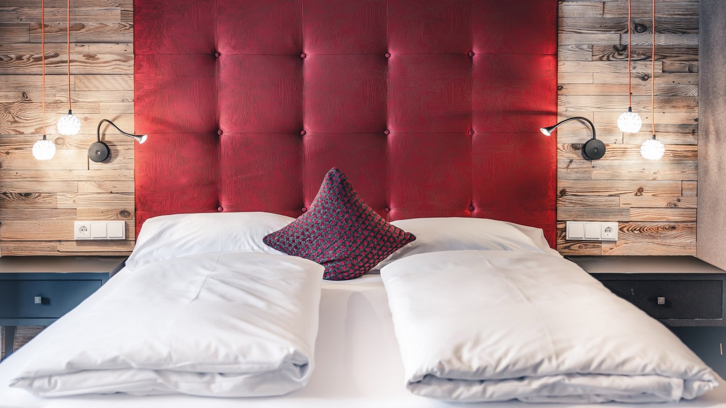 Hotel Sonnenhof Gemachtes Bett mit roten Kopfteil, graurotem Kissen und Holzwand
