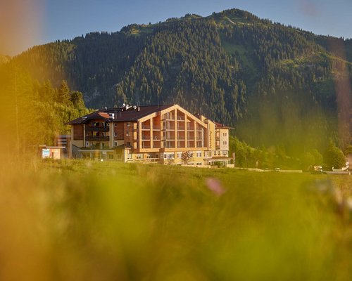 Hotel Sonnenhof umgeben von Almwiesen Berghotel mit Wiese im Vordergrund und bewaldetem Berg im Hintergrund bei Sonnenschein