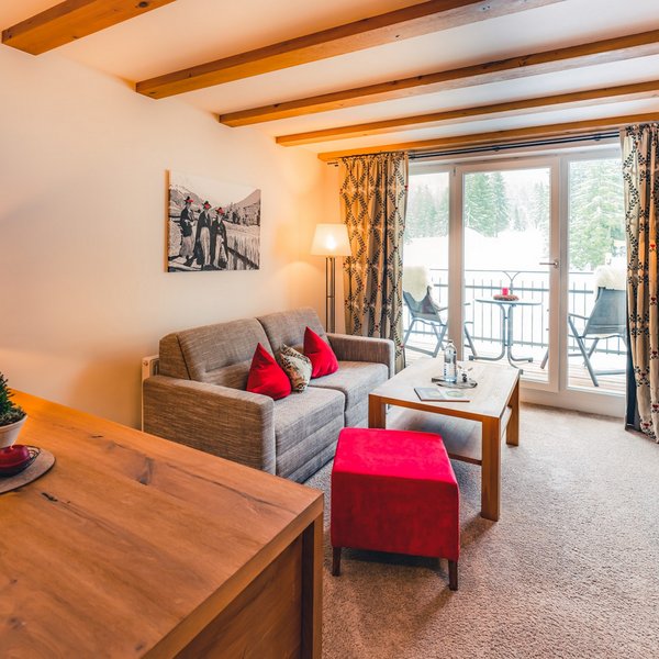 Hotel Sonnenhof Gemütliches Wohnzimmer mit Sofa, rotem Hocker und Blick auf verschneite Landschaft