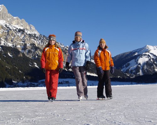 Hotel Sonnenhof Drei Kinder beim Eislaufen auf gefrorenem See mit Bergen im Hintergrund