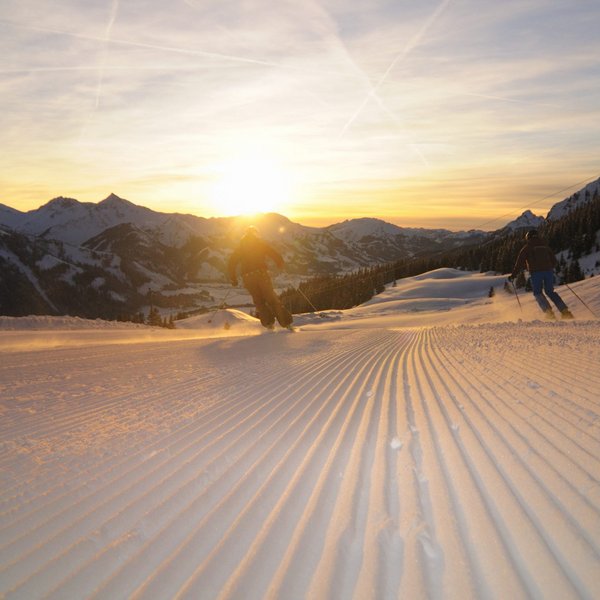 Hotel Sonnenhof Skifahrer fahren bei Sonnenuntergang auf frisch präparierter Piste in den Bergen