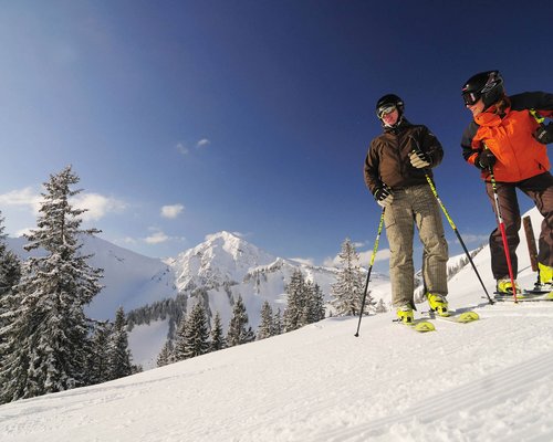 Hotel Sonnenhof Zwei Skifahrer auf schneebedecktem Hang mit Bergen und Bäumen im Hintergrund