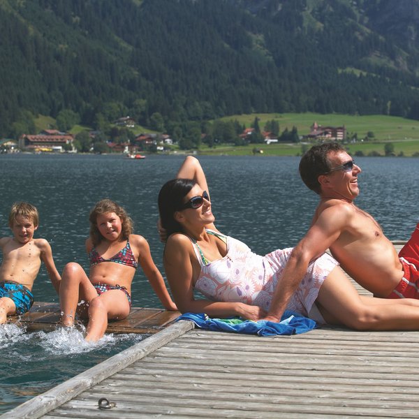 Hotel Sonnenhof Familie entspannt am Seeufer auf Steg mit Bergen und Häusern im Hintergrund