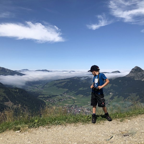 Hotel Sonnenhof Junge mit Kamera steht auf Bergpfad mit Blick auf Tal und Wolken