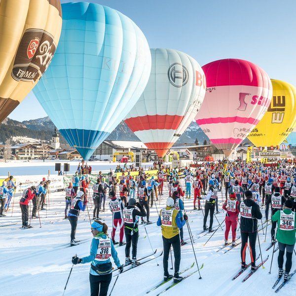 Hotel Sonnenhof Skilangläufer starten im Schnee unter bunten Heißluftballons bei klarem Himmel
