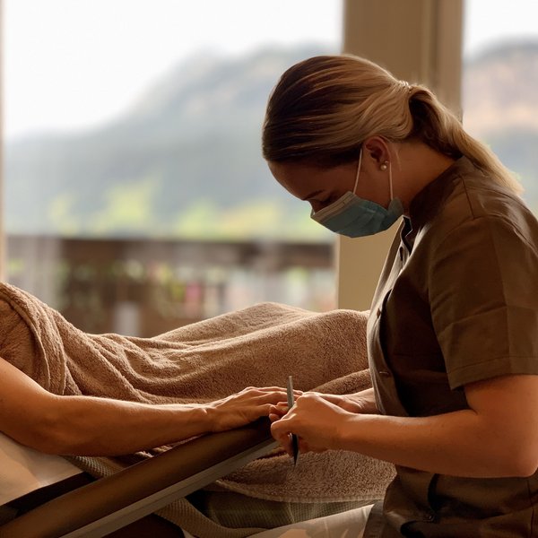 Hotel Sonnenhof Frau mit Maske macht Maniküre während Kunde entspannt auf Liegestuhl liegt